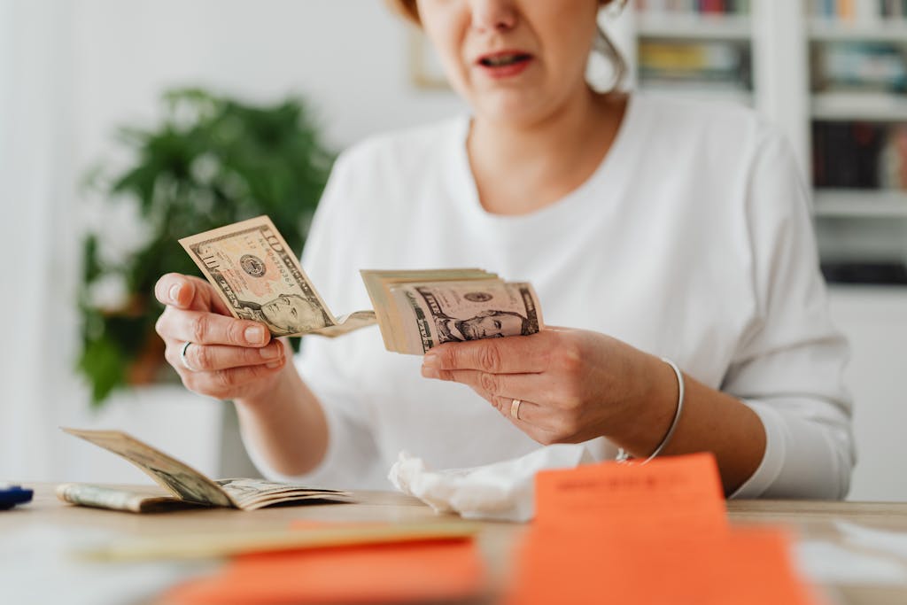 A woman sits indoors counting cash at her office desk, focusing on finances.